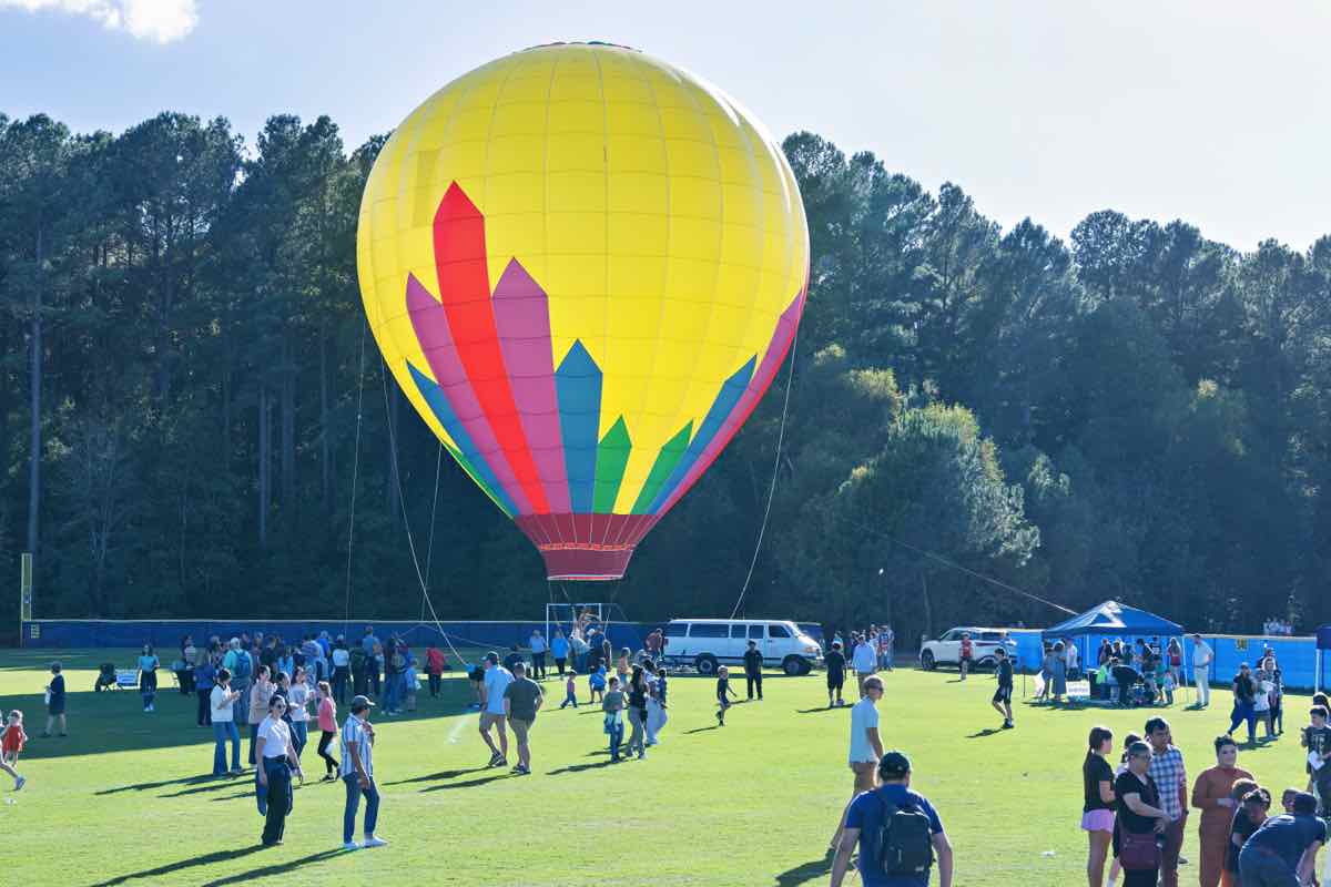 A tethered yellow hot air balloon above the crowd on the athletic field