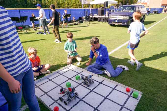 Students steering robots across a game board on the athletic field
